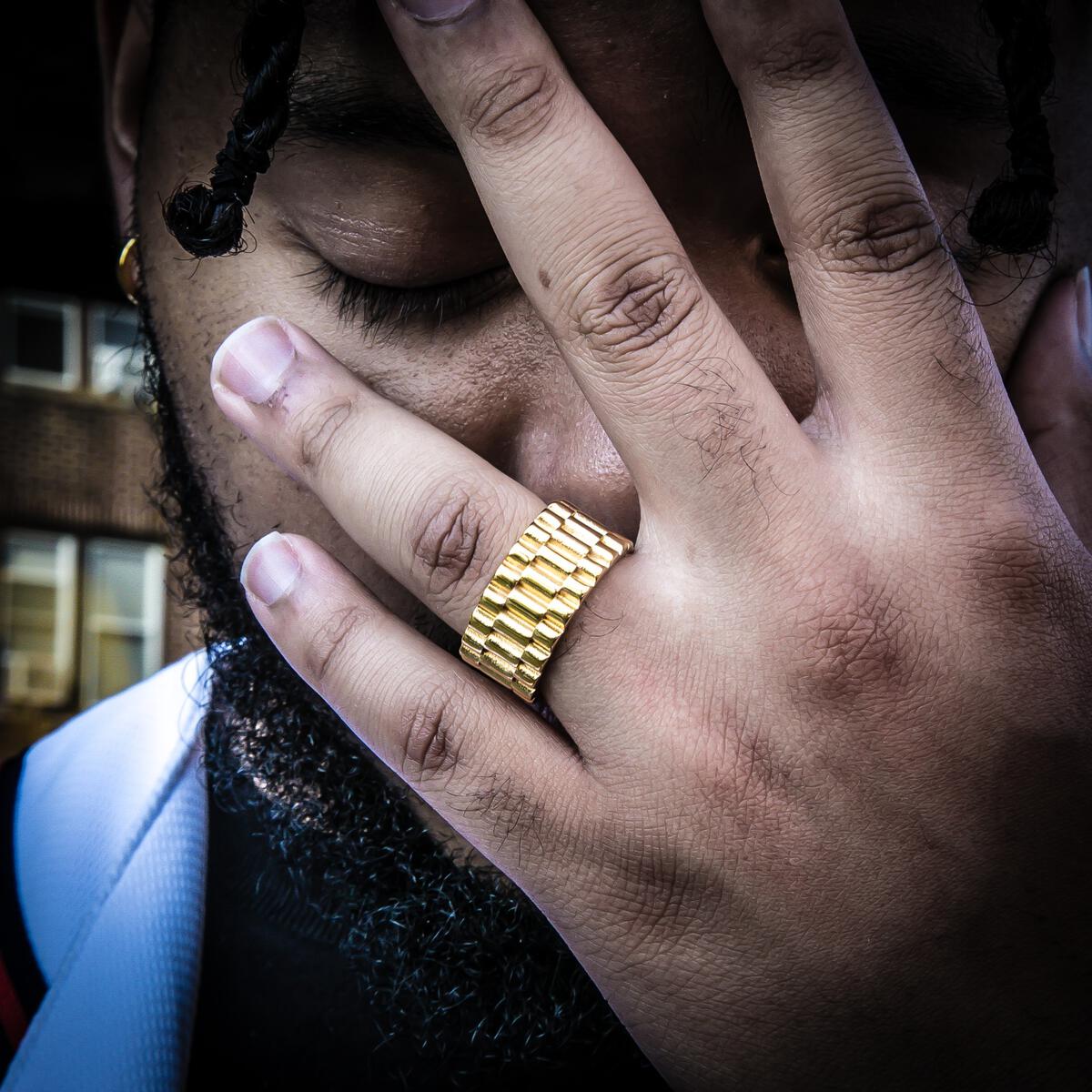 Close-up of a hand wearing the gold presidential ring covering a person's face outdoors.