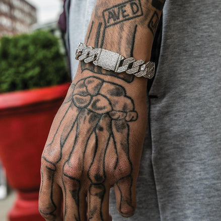 Hand with tattoos wearing the silver prong cuban link bracelet on a blurred background