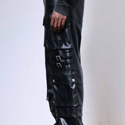 Person wearing black leather pants with multiple pockets and buckles on a plain background