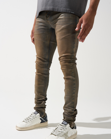 Person wearing brown skinny jeans and white sneakers on a white background