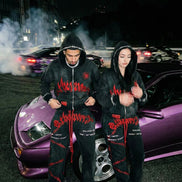 Two people in matching outfits standing next to a purple car at night.