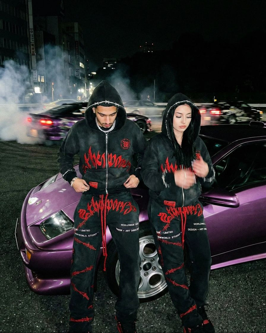 Two people in matching outfits standing next to a purple car at night.