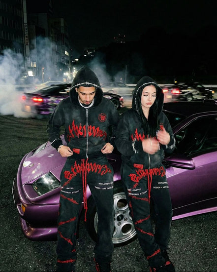 Two people in matching outfits standing next to a purple car at night.