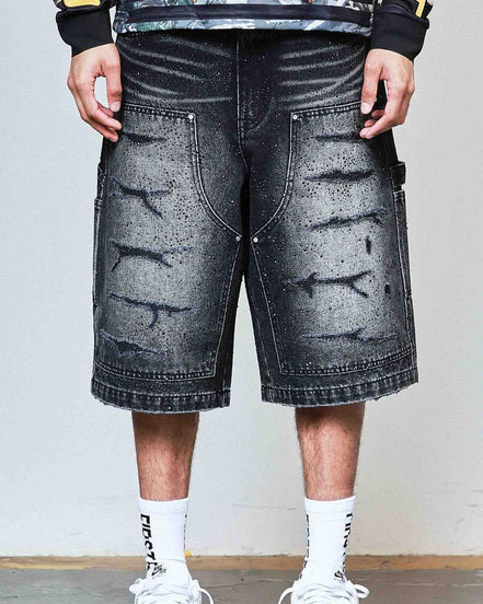 Person wearing black distressed denim shorts with a plain background