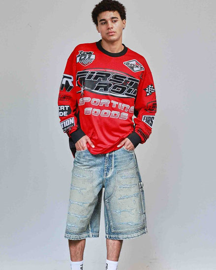 Person wearing a red sweatshirt with branding and denim shorts on a plain background