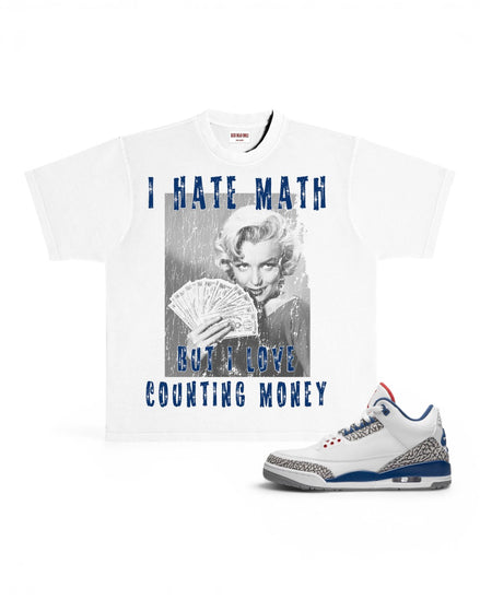 A white graphic t-shirt featuring a black-and-white photo of Marilyn Monroe holding cards with blue text reading 'I HATE MATH BUT I LOVE COUNTING MONEY', shown next to a white sneaker with blue and gray accents on a white background.