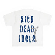 A white short-sleeve t-shirt with a graphic print on the front. The design features the text 'RICH DEAD IDOLS' in a distressed blue font, with a gray silhouette of Marilyn Monroe holding a microphone integrated into the lettering.