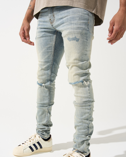 Person wearing light blue distressed jeans and white sneakers with black stripes on a white background