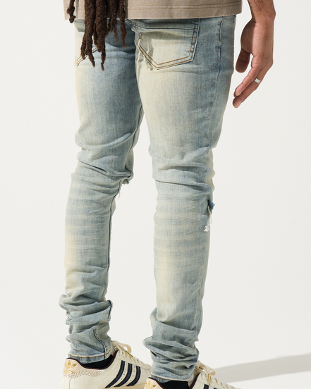 Person wearing light blue jeans and white sneakers with black stripes on a white background