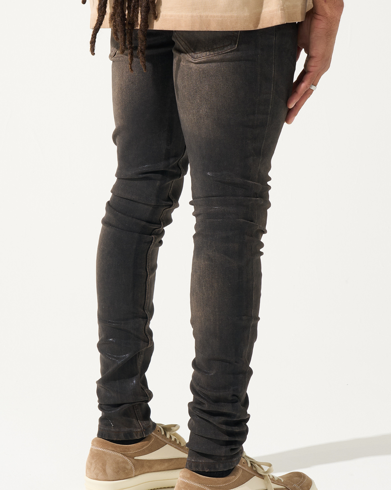 Person wearing dark distressed jeans and brown shoes on a white background