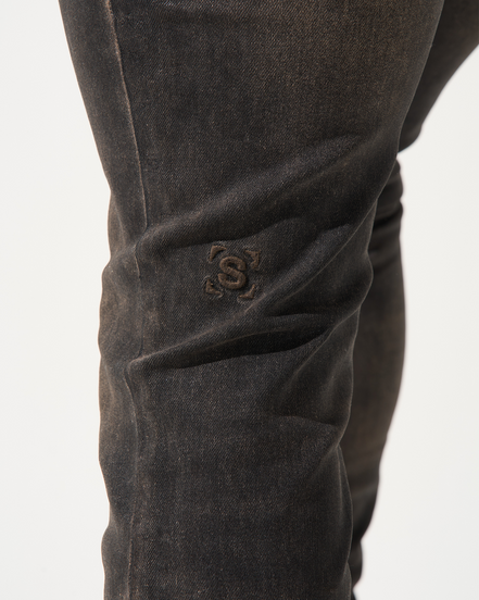 Close-up of dark brown pants with a brand logo on a white background
