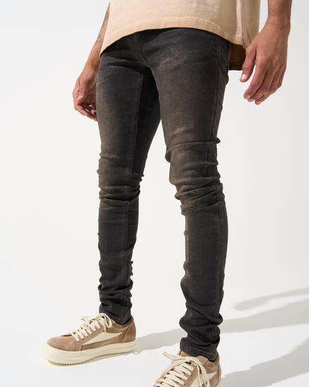 Person wearing dark distressed jeans and beige sneakers on a white background