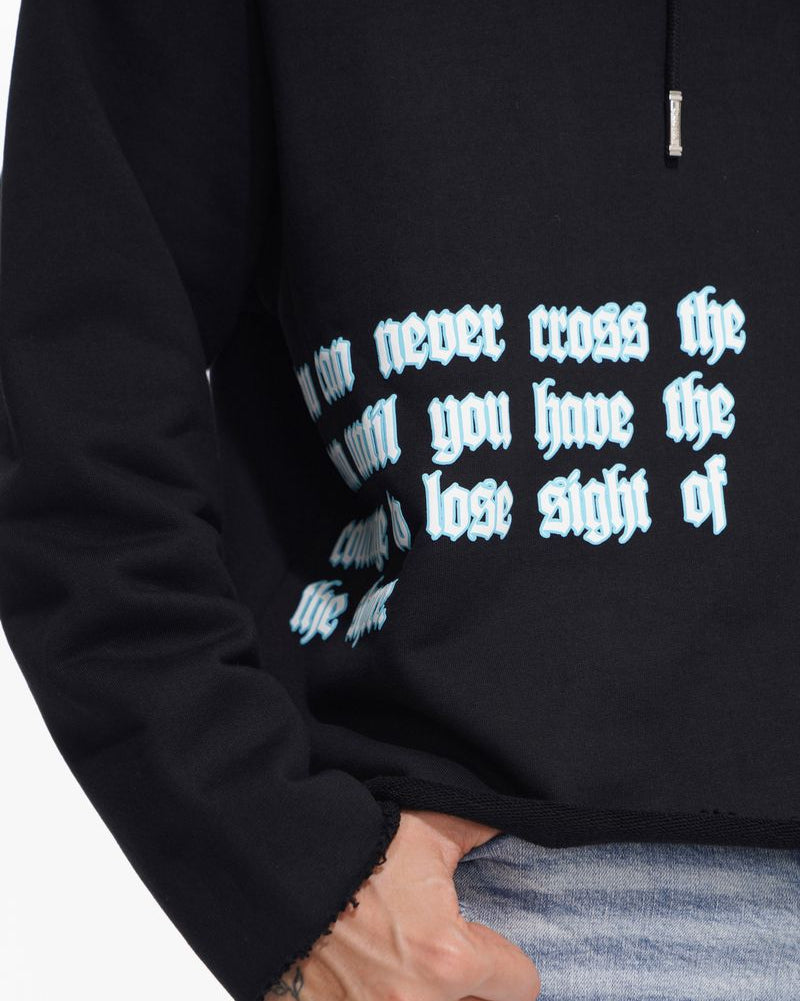 Black hoodie with reflective text worn by a person, with jeans visible.