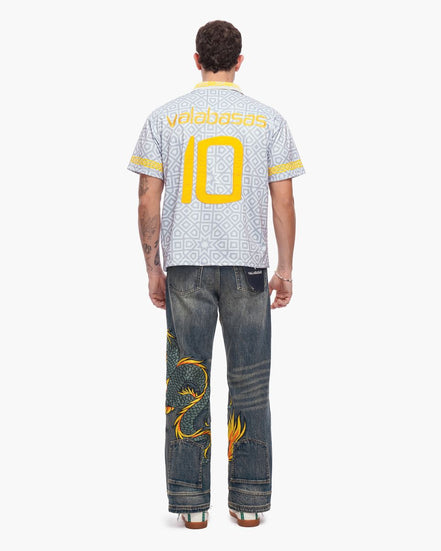 Person wearing a white sports jersey with yellow numbers and text, paired with blue jeans featuring gold designs.