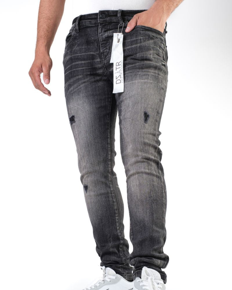 Person wearing black distressed jeans with a tag, standing on a white background