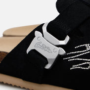 Black sneaker with a silver bottle opener attached to the tongue on a white background