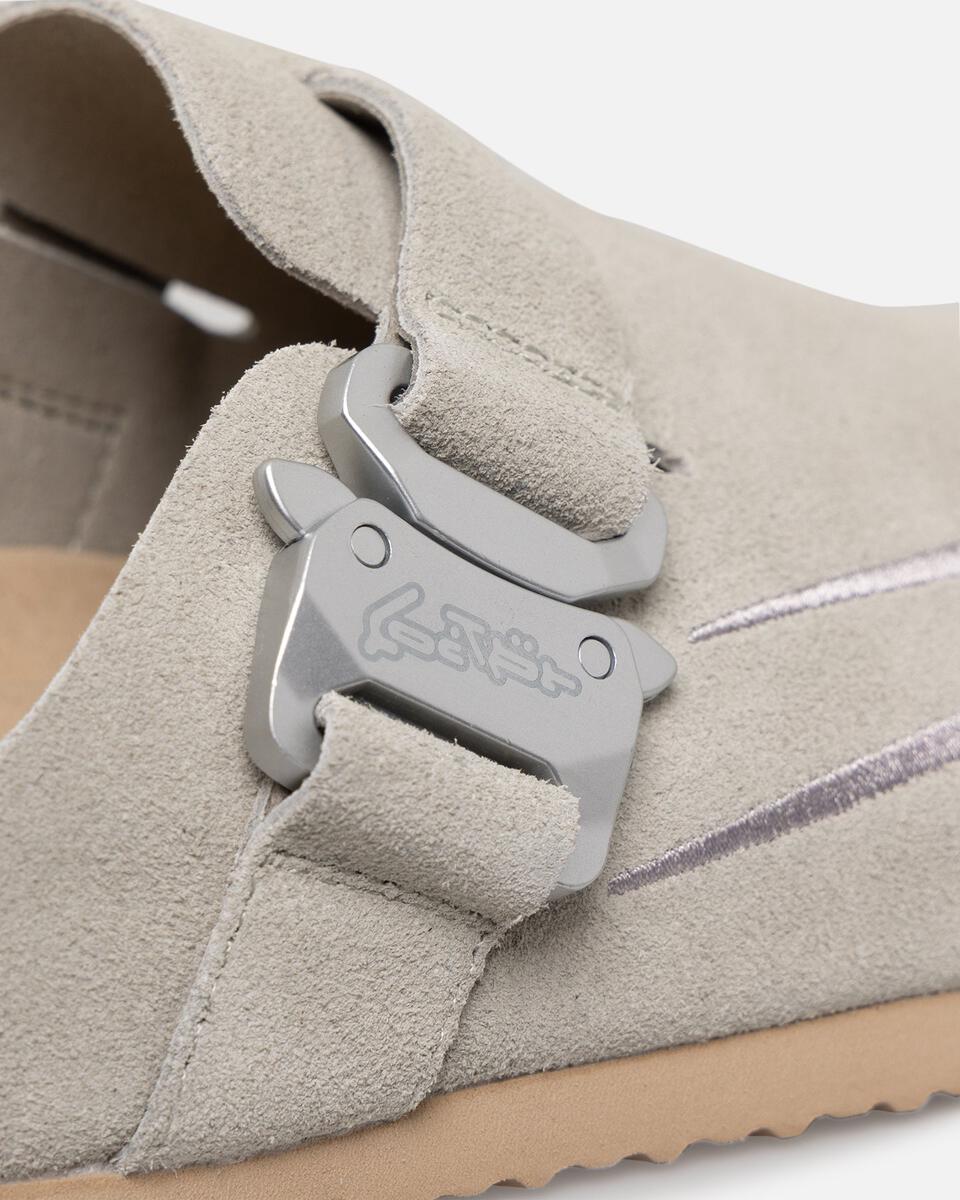 Close-up of a beige suede shoe with a metal buckle on a light gray background