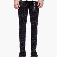 Black glittery pants with a brand logo worn by a person on a white background