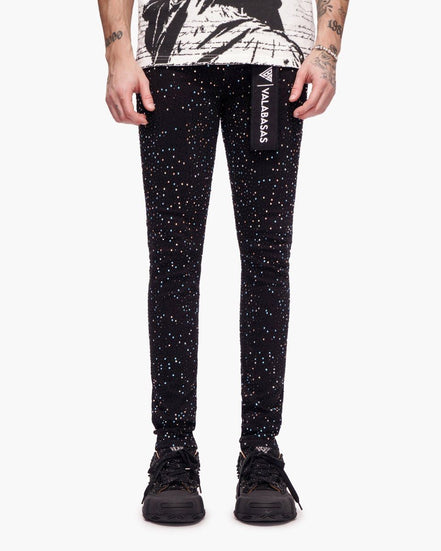 Black glittery pants with a brand logo worn by a person on a white background
