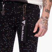 Person wearing black pants with white polka dots, holding a black pouch with 'VALABASAS' branding.