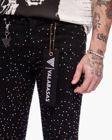 Person wearing black pants with white polka dots, holding a black pouch with 'VALABASAS' branding.