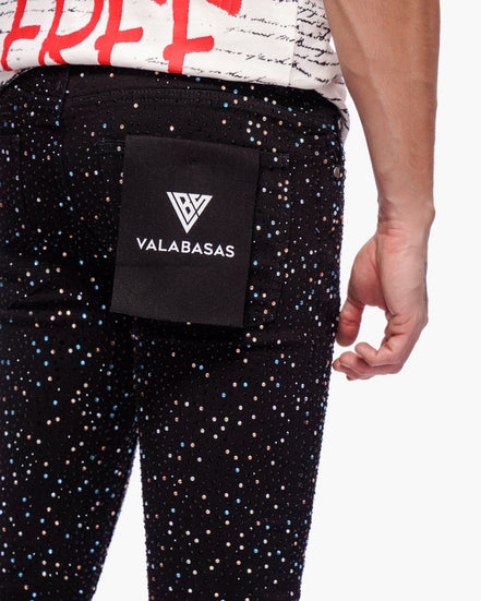 Person wearing black pants with multicolor dots and a black waist bag with 'VALABASAS' branding.