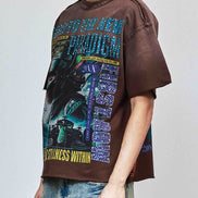 Person wearing a brown graphic t-shirt with a colorful design and ripped jeans on a plain background