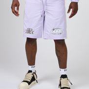 A person wearing light lavender Nike shorts with white side stripes and silver logo graphics, paired with white socks and beige-and-black sneakers, photographed against a light gray studio background.