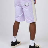 A person shown from the waist down wearing light lavender shorts with a cream side stripe and a moon graphic on the back pocket, paired with white socks and black sneakers, against a light gray studio background.
