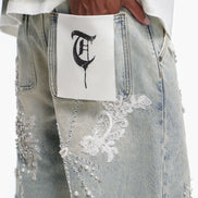 Person wearing a white shirt with text, light blue jeans with lace details, and a white pouch with a black design.