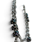 A silver-toned chain accessory with multiple black faceted beads that shimmer with iridescent rainbow reflections, photographed on a clean white background.