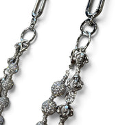 Close-up of a silver-toned jewelry accessory with a lobster clasp and dangling beaded chain details on a white background.