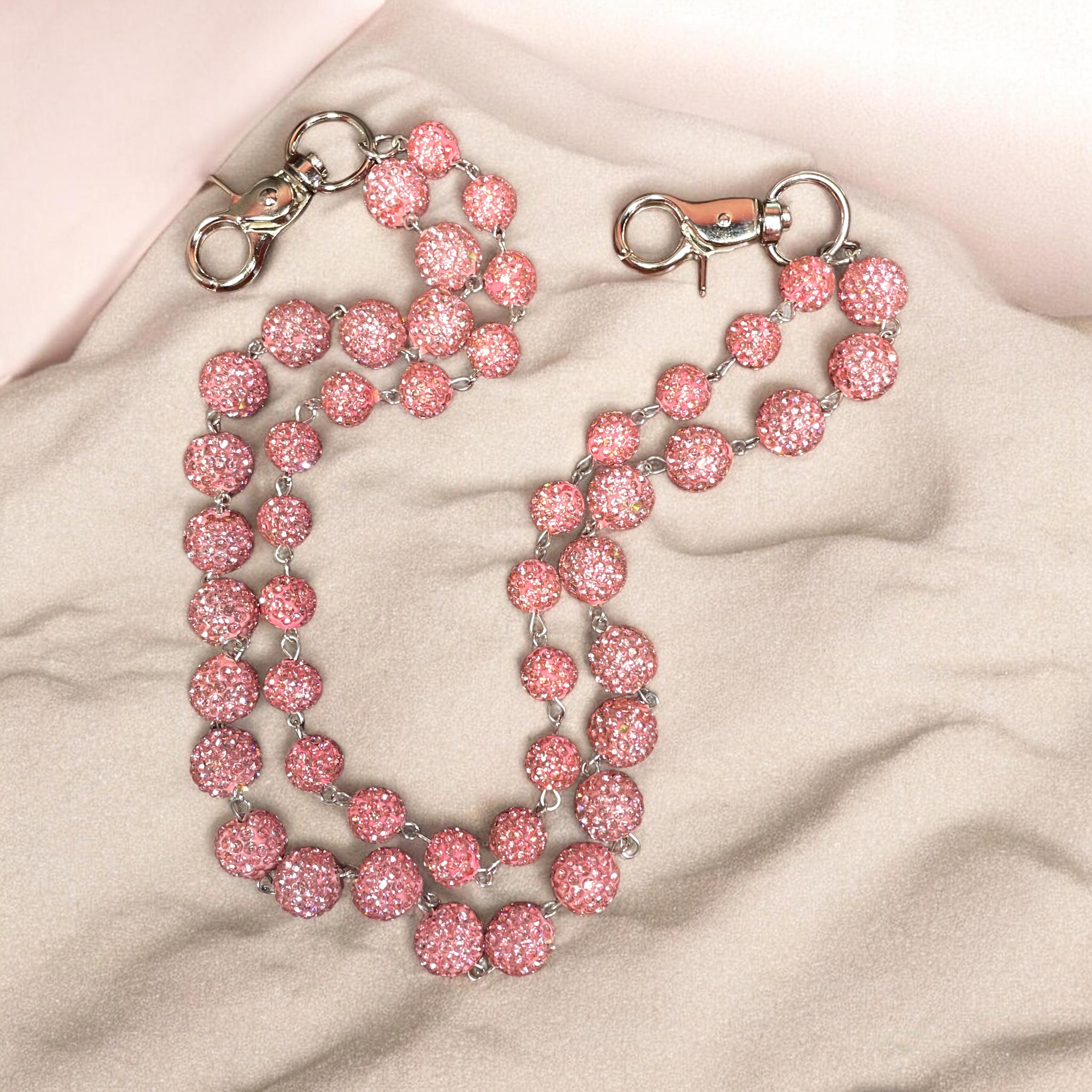 Pink beaded wallet chain with metal clasps on a beige fabric background