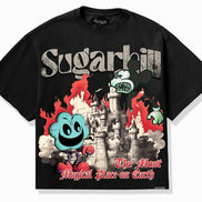 A black short-sleeve graphic T-shirt laid flat against a light gray background. The front features a large multicolor print with the word 'Sugarhill' in distressed white lettering, a gray castle, red flames, a blue smiling ghost-like character, and red script text reading 'The Most Magical Place on Earth.