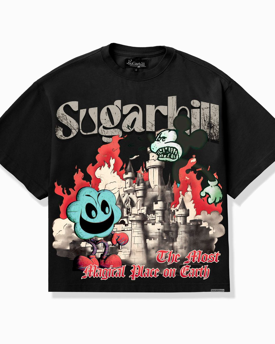 A black short-sleeve graphic T-shirt laid flat against a light gray background. The front features a large multicolor print with the word 'Sugarhill' in distressed white lettering, a gray castle, red flames, a blue smiling ghost-like character, and red script text reading 'The Most Magical Place on Earth.