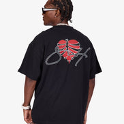 A man wearing a black oversized t-shirt from the back, featuring a red heart graphic with a basketball design and a white script logo. He is also wearing gray jeans, a silver chain necklace, and white-framed sunglasses against a light gray background.
