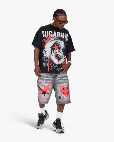 A man modeling a black graphic t-shirt with 'SUGARHILL' text and a clown print, paired with gray distressed shorts featuring red smiley face graphics, white socks, and black sneakers, against a light gray background.