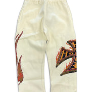 Off-white sweatpants featuring a red and black flame graphic on the left leg and a large black and orange graphic with red flame details on the right leg, displayed flat against a white background.