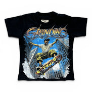 A black short-sleeve graphic t-shirt featuring a large front print of a skateboarder in mid-air above a city skyline, with the word 'GRINDING' in stylized metallic lettering. The shirt is displayed flat against a plain white background.