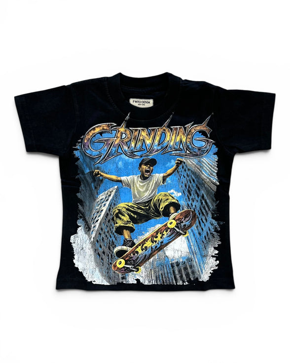 A black short-sleeve graphic t-shirt featuring a large front print of a skateboarder in mid-air above a city skyline, with the word 'GRINDING' in stylized metallic lettering. The shirt is displayed flat against a plain white background.