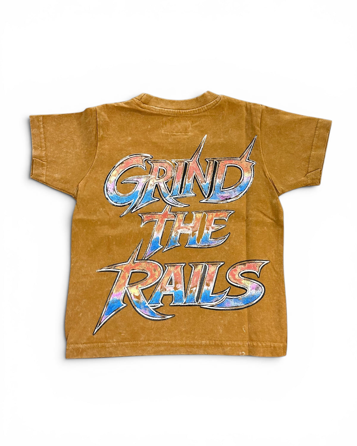 A short-sleeve crewneck t-shirt in a washed, mustard-brown color, featuring a large graphic print on the back that reads 'GRIND THE RAILS' in a stylized metallic font with blue, red, and silver colors.