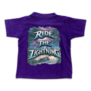 A purple short-sleeve t-shirt shown from the back, featuring a large graphic print with the text 'RIDE THE LIGHTNING' in stylized blue and white lettering over a smoky, lightning-themed background.
