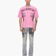 Person wearing a pink t-shirt with graphic design and patterned pants on a white background