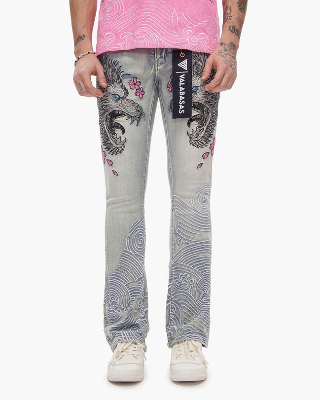 Person wearing gray jeans with intricate designs and a pink top on a white background