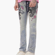 Person wearing gray jeans with floral and abstract designs, white sneakers, and a pink top on a white background.