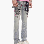 Person wearing blue jeans with floral and eagle design, pink shirt, and white sneakers on a white background