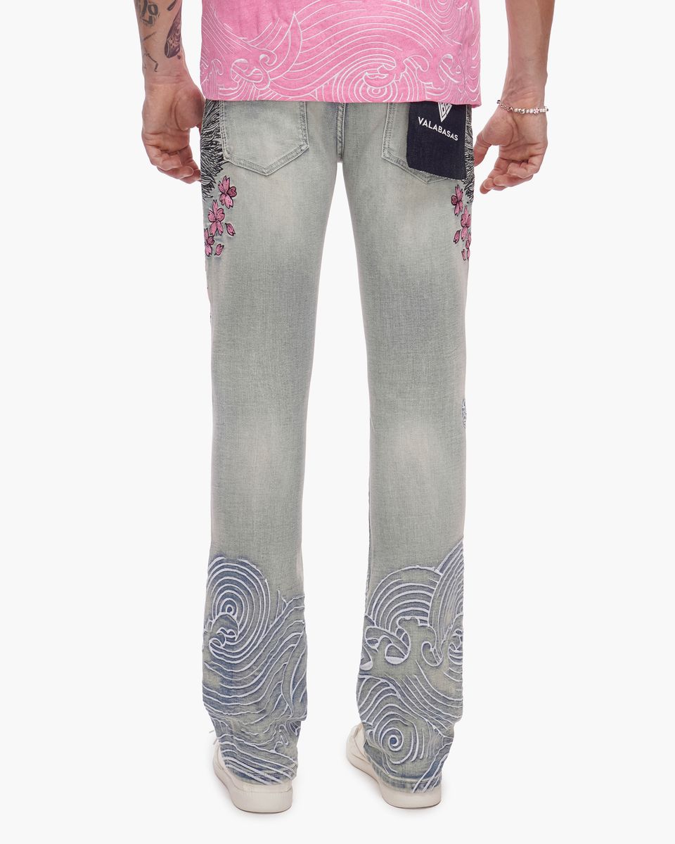 Person wearing light blue jeans with decorative patterns on a white background