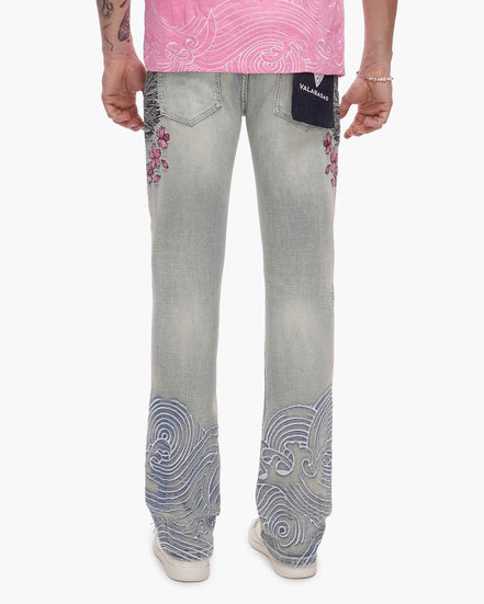 Person wearing light blue jeans with decorative patterns on a white background