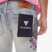 Close-up of a person wearing light blue jeans with a 'VALABASAS' label on the back pocket, pink shirt, and floral designs.
