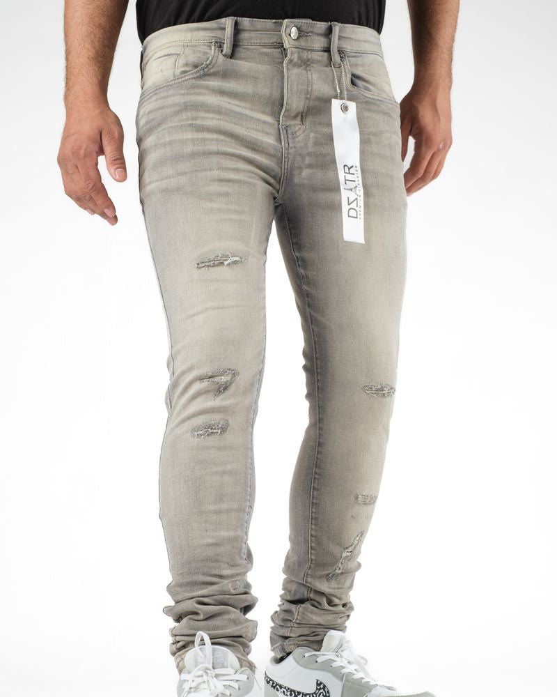 Person wearing light gray distressed jeans with a brand tag, standing against a white background